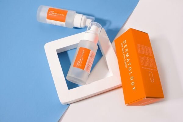 Stylish presentation of dermatology skincare products with orange packaging on a geometric background.